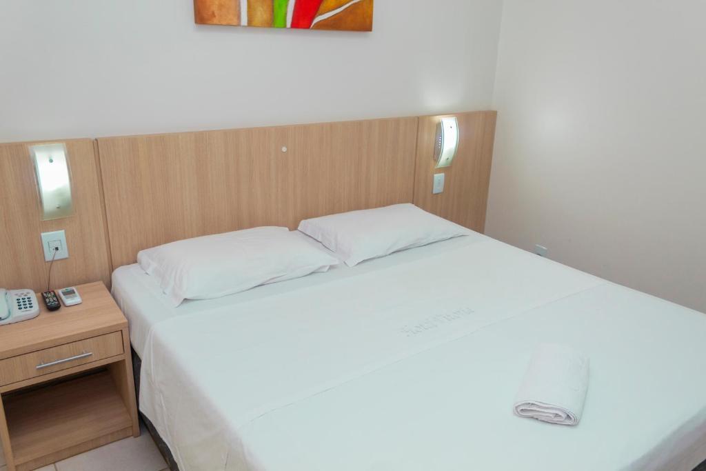 - une chambre avec un grand lit blanc et un téléphone dans l'établissement Hotel Vitoria - Itajaí, à Itajaí