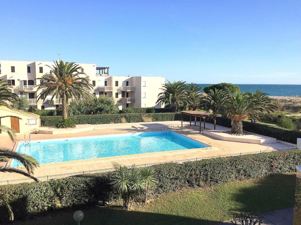 une piscine avec des palmiers devant un immeuble dans l'établissement Résidence Les Capitelles à Saint Cyprien avec accès direct plage- Balcon donnant Splendide vue Mer et Piscine, à Saint-Cyprien