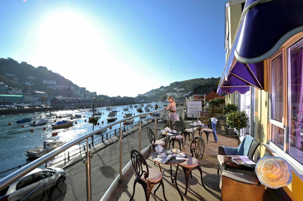 a woman standing on a balcony overlooking a river with boats at The Old Bridge House in Looe