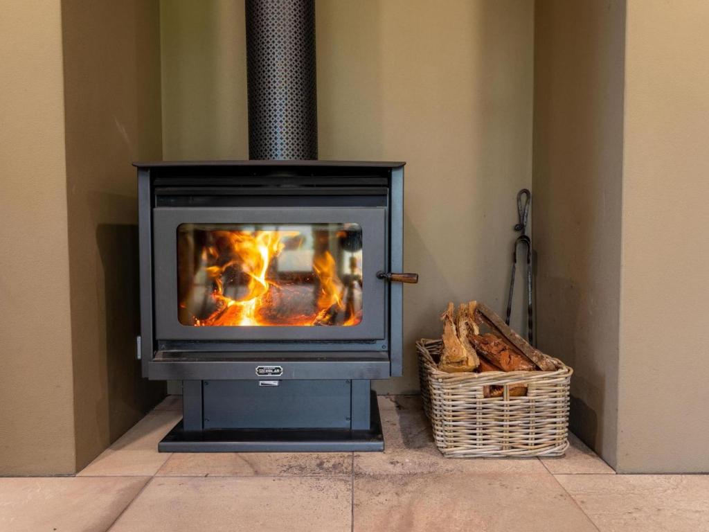 a stove in a room with a basket of logs at The Dairy at Cavan I Kangaroo Valley I Stunning Views in Barrengarry