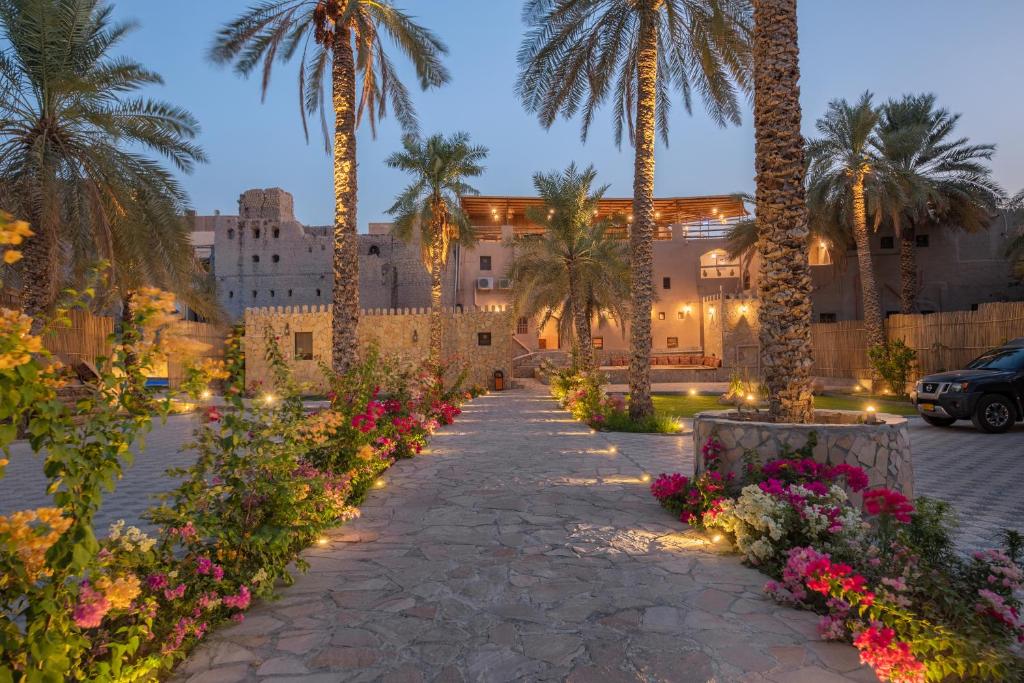 a pathway with palm trees and flowers in front of a building at Antique Inn in Nizwa