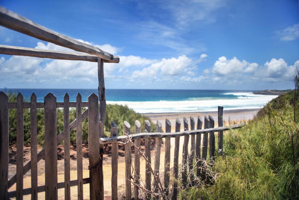 a wooden fence next to a beach with the ocean at Tofinho Beach House in Praia do Tofo