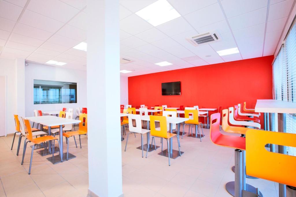 a dining room with tables and chairs and a red wall at Premiere Classe Caen Nord - Mémorial in Caen