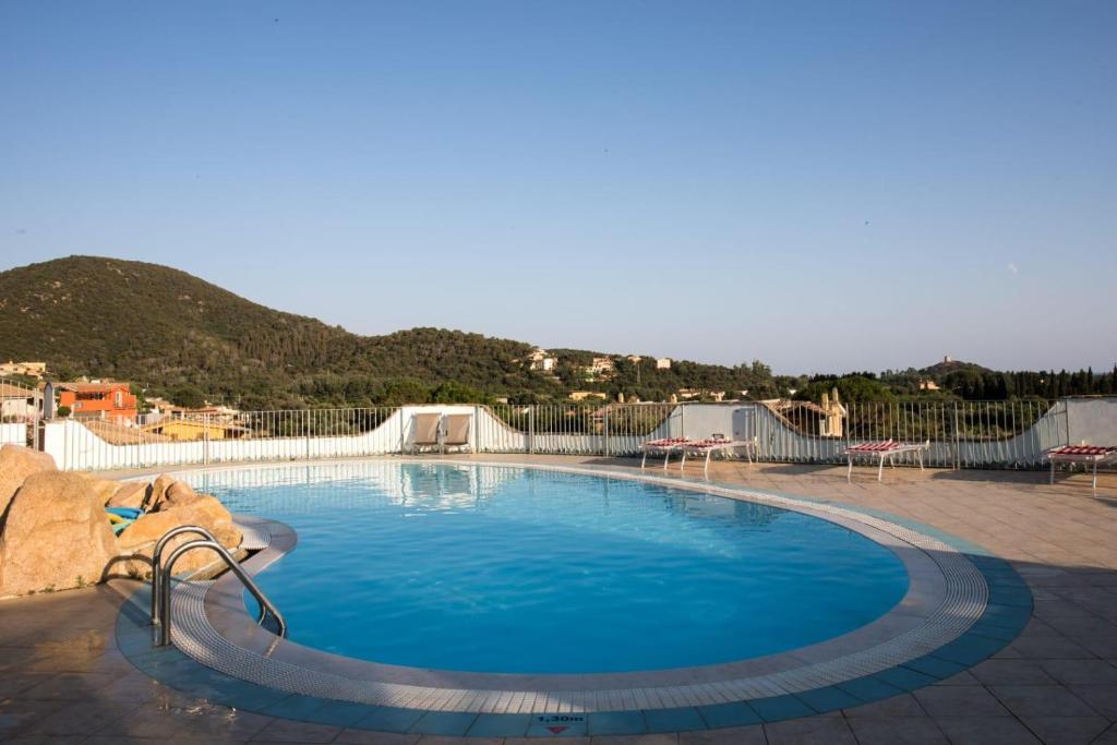 a large blue swimming pool with a mountain in the background at Sobìa Manna in Chia