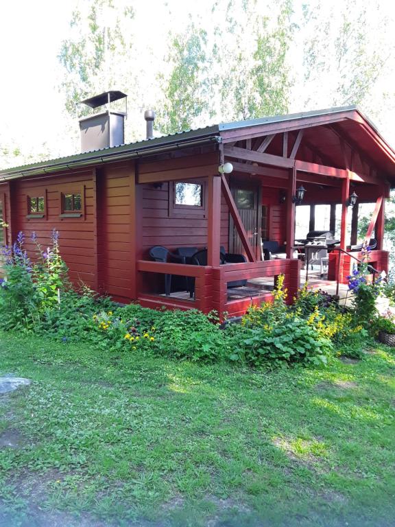 a red cabin with a porch and a grass field at Rantapuro in Alvajärvi