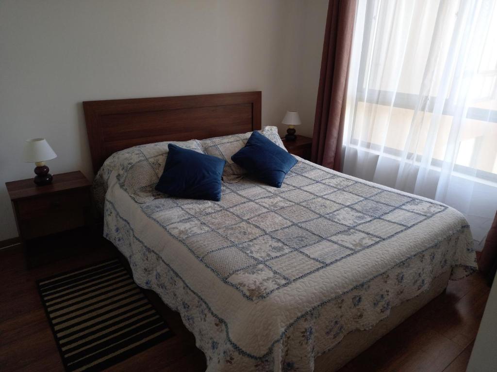 a bedroom with a bed with blue pillows and a window at Departamento Ricardo in Viña del Mar