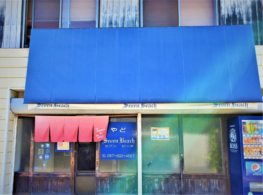 Przednia część sklepu z niebieską markizą na budynku w obiekcie Yado Seven Beach w mieście Naoshima