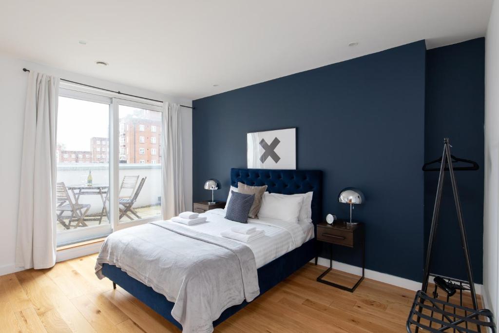 a blue bedroom with a bed with a blue accent wall at London City Apartments - Luxury and spacious apartment with balcony in London