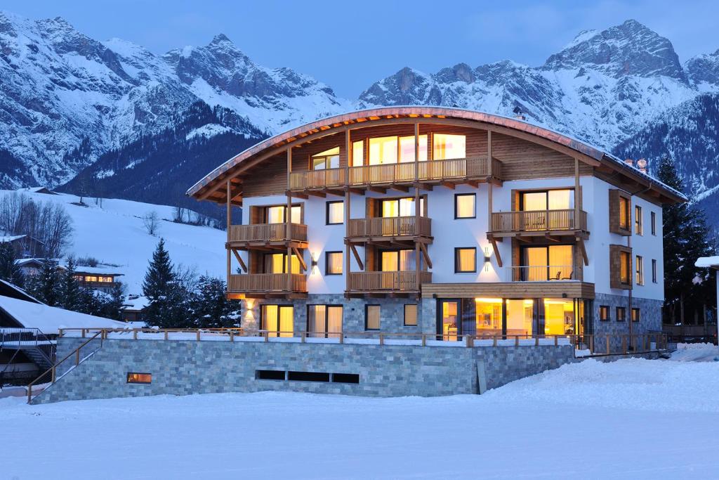 a large building in the snow with mountains at Sunnsait - Appartements für Genießer in Maria Alm am Steinernen Meer