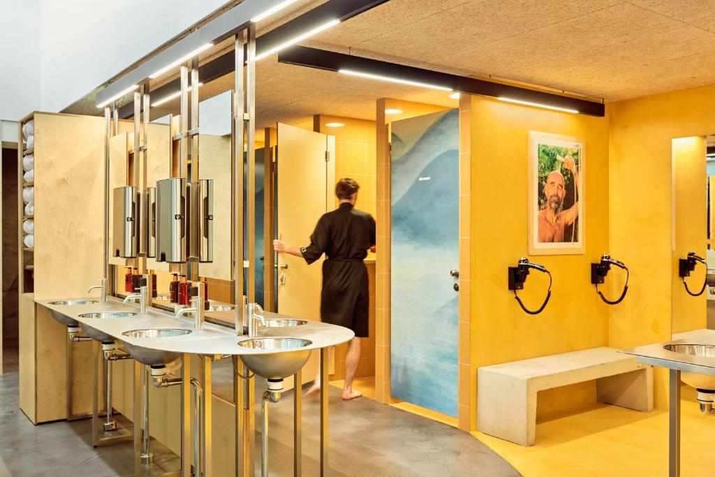 a woman standing in a bathroom with four sinks at CityHub Copenhagen in Copenhagen