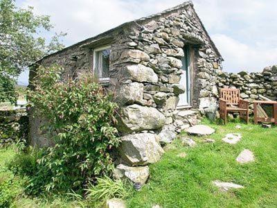 an old stone house with a bench and a chair at The Bothy at Woodend with Views of Scafell in Broughton in Furness