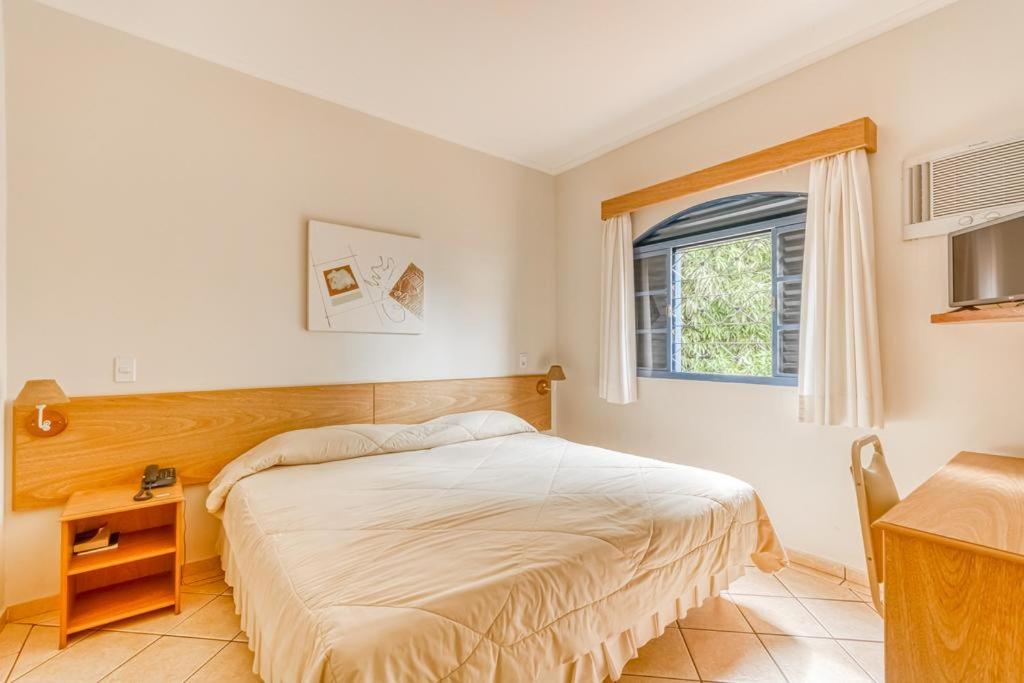 Schlafzimmer mit einem Bett, einem Fenster und einem Tisch in der Unterkunft Jardin Park Hotel in Jardinópolis