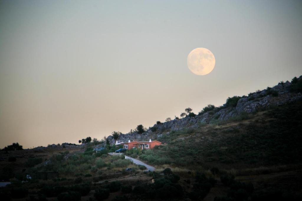 Cortijo Nuevo Alojamiento Rural في Cuevas del Becerro: صعود قمر كامل فوق منزل على تلة