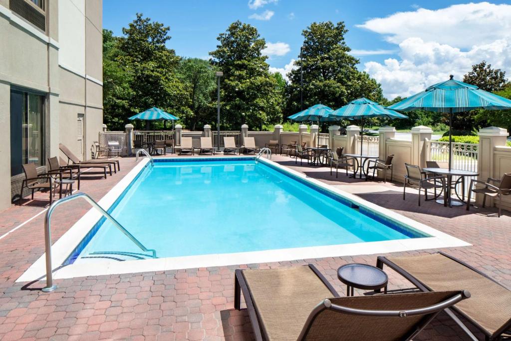 uma piscina com cadeiras, mesas e guarda-sóis em Hyatt Place Charlotte Arrowood em Charlotte