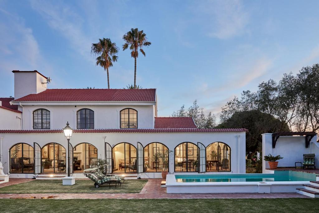 a large white house with a pool and palm trees at Deux Frères Wine Estate & Luxury Villas in Stellenbosch
