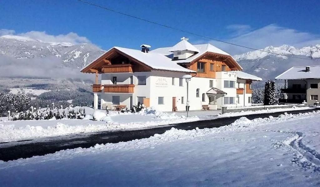 a house in the snow with mountains in the background at Residence Stefansdorf in Brunico