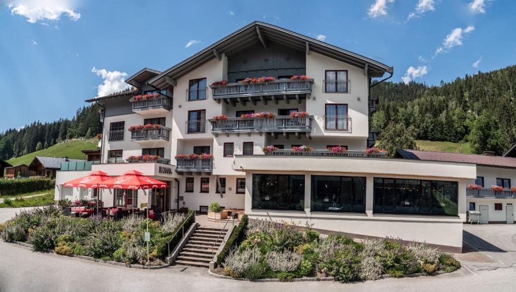 ein großes weißes Gebäude mit roten Sonnenschirmen davor in der Unterkunft Hotel Sonnschupfer in Schladming
