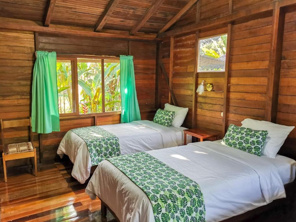 two beds in a room with wooden walls and windows at Cabañas Germany in Puyo