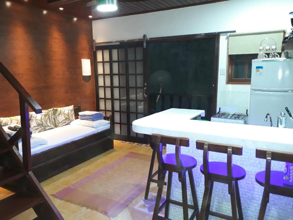 eine Küche mit einer Bar mit lila Hockern und einer Couch in der Unterkunft Angel Ilha Flats e Varanda da Praia in Abraão