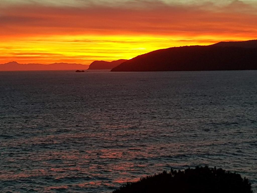 un tramonto sull'oceano con montagne sullo sfondo di Appartamenti La Conchiglia a Capoliveri