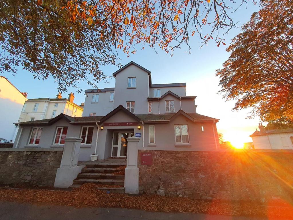een groot wit huis met de zonsondergang erachter bij The Maycliffe Hotel in Torquay