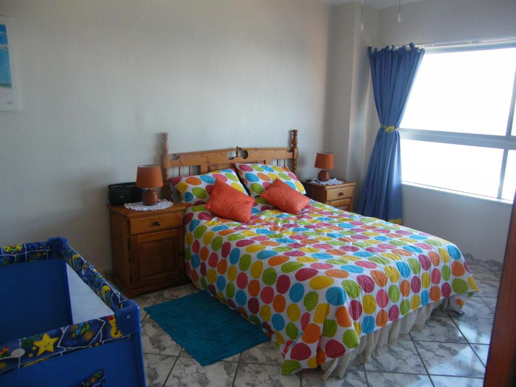 a bedroom with a bed with colorful sheets and a window at 1102 High Tide Amanzimtoti in Amanzimtoti