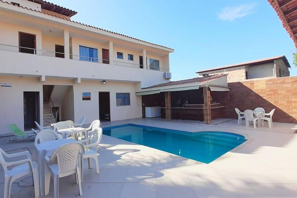 Villa con piscina y sillas blancas en Casa Paraná com 8 quartos com área gourmet, en Porto Seguro