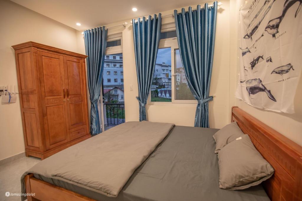 a bedroom with a bed and a window with blue curtains at Nhà của Sóc in Da Lat