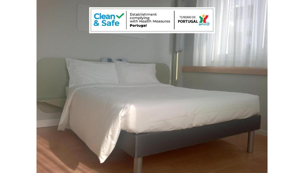 łóżko z białą pościelą i poduszkami w pokoju w obiekcie Ibis Budget Braga Centro w mieście Braga