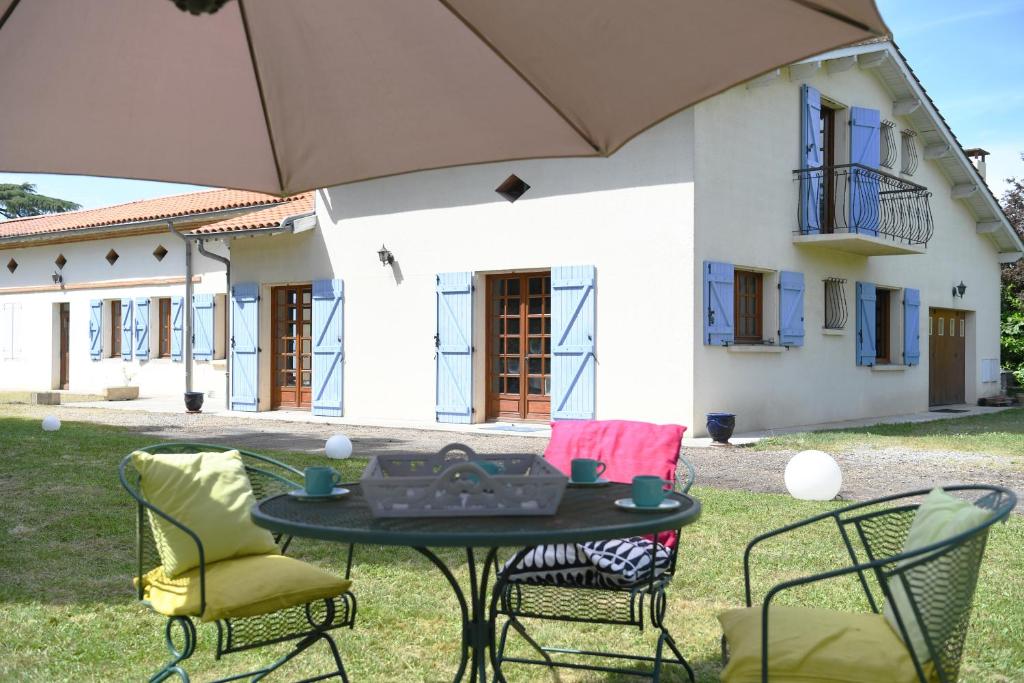a table with chairs and an umbrella in front of a house at Maison de campagne sud-ouest CARBONNE en OCCITANIE in Carbonne
