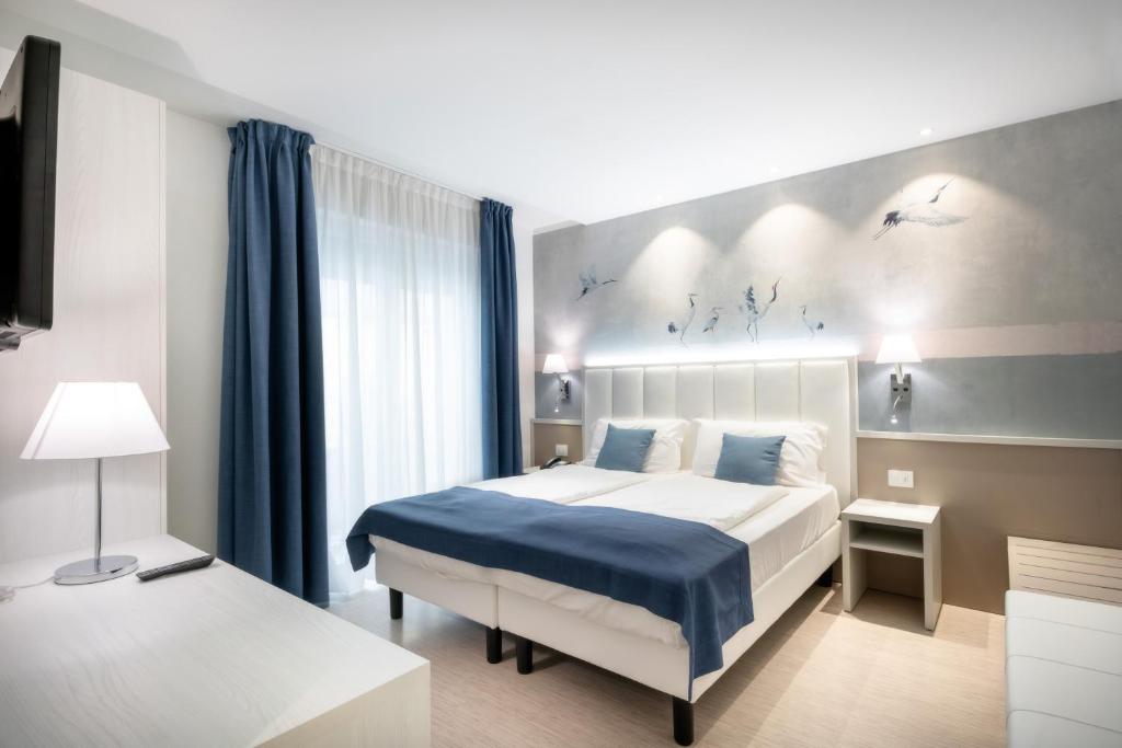 a bedroom with a large bed with blue sheets and blue curtains at International Beach Hotel in Caorle
