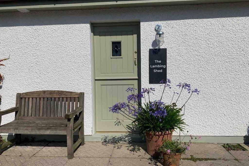 um banco de madeira em frente a um edifício com uma porta em The Lambing Shed em Bushmills