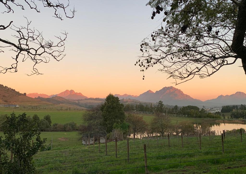 einen Sonnenuntergang über einem Feld mit einem Fluss und Bergen in der Unterkunft Wildlife Retreat on a Wine-Farm in Stellenbosch