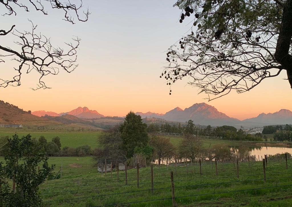 a sunset over a field with a river and mountains at Wildlife Retreat on a Wine-Farm in Stellenbosch