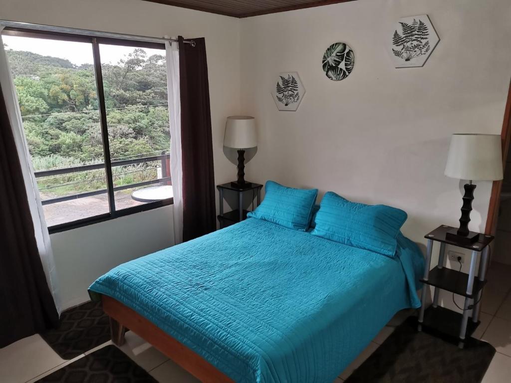 Un dormitorio con una cama azul y una ventana en Hostel Coati Place Bed & Breakfast Adults Only, en Monteverde
