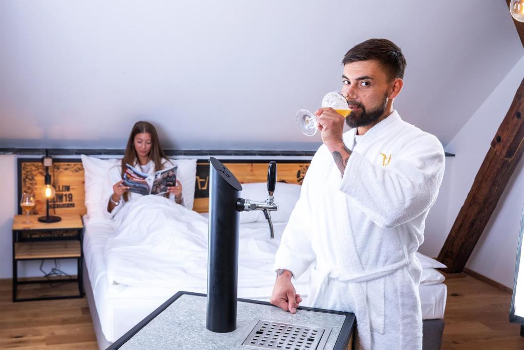 a man drinking a glass of wine next to a bed at Pivní Hotel in Nepomuk