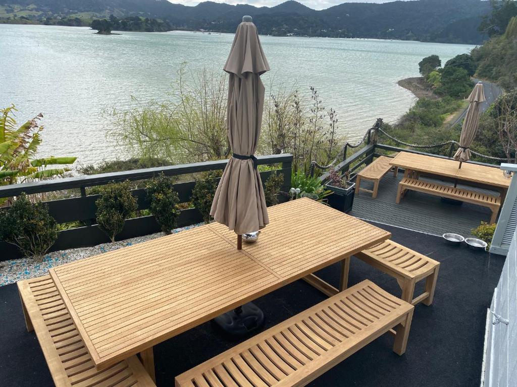 une table en bois avec un parasol sur une terrasse à côté de l'eau dans l'établissement Pacific Harbour Lodge, à Whangaroa