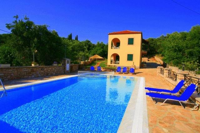 a swimming pool with blue chairs and a house at Emily's Apartments in Kassiopi