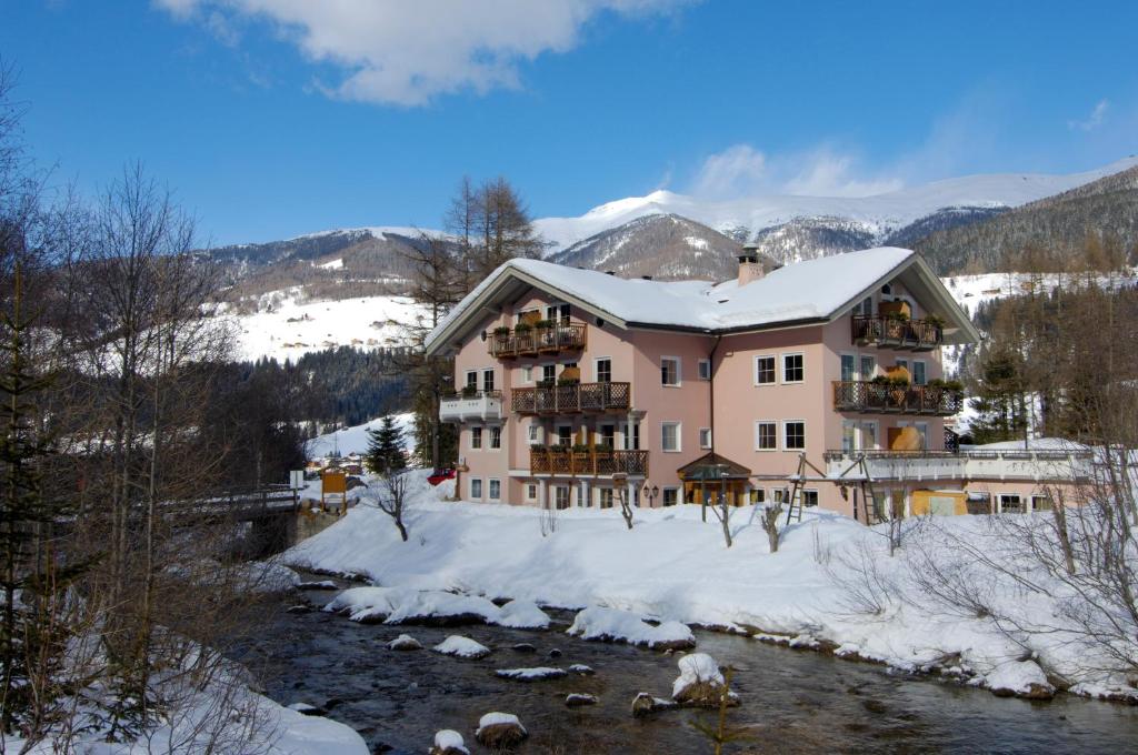 a large pink building in the snow next to a river at BAD MOOS Dependance "Mühlenhof" in Sesto
