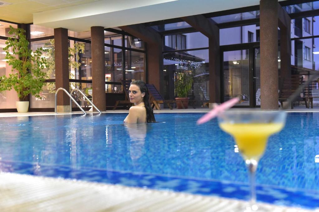 een vrouw in een zwembad met een drankje bij Royal Bansko - Half Board Plus & All Inclusive - Hot Pool & Jacuzzis in Bansko