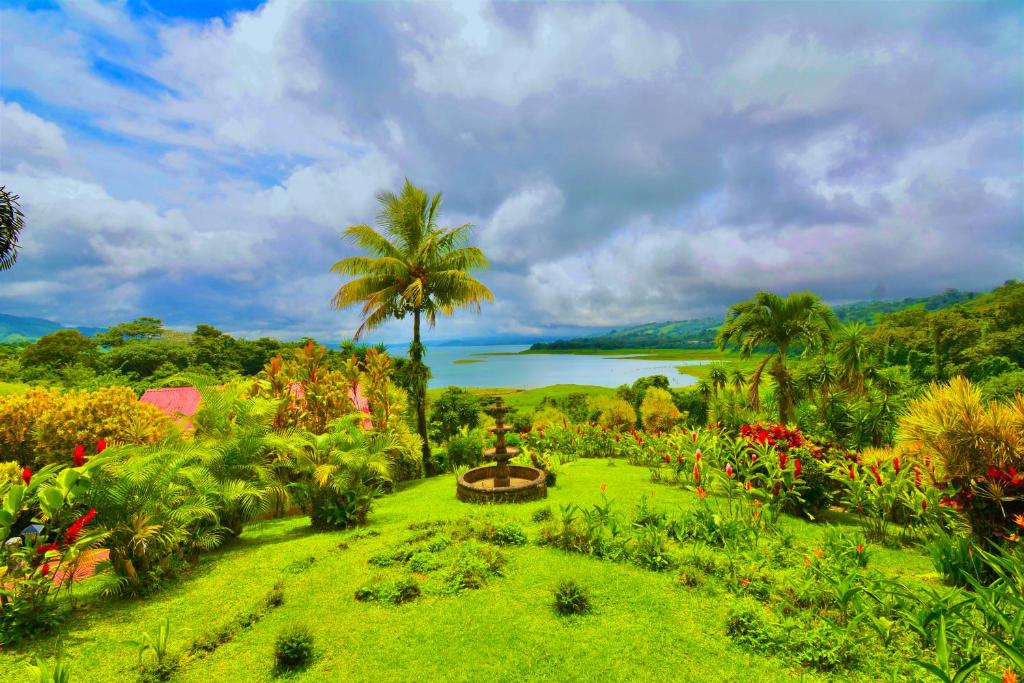 a garden with a palm tree and a lake at Hotel La Mansion Inn Arenal in Nuevo Arenal