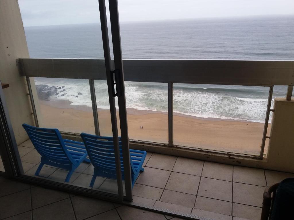 two blue chairs sitting on a balcony looking out at the beach at 197 Stella Maris in Amanzimtoti