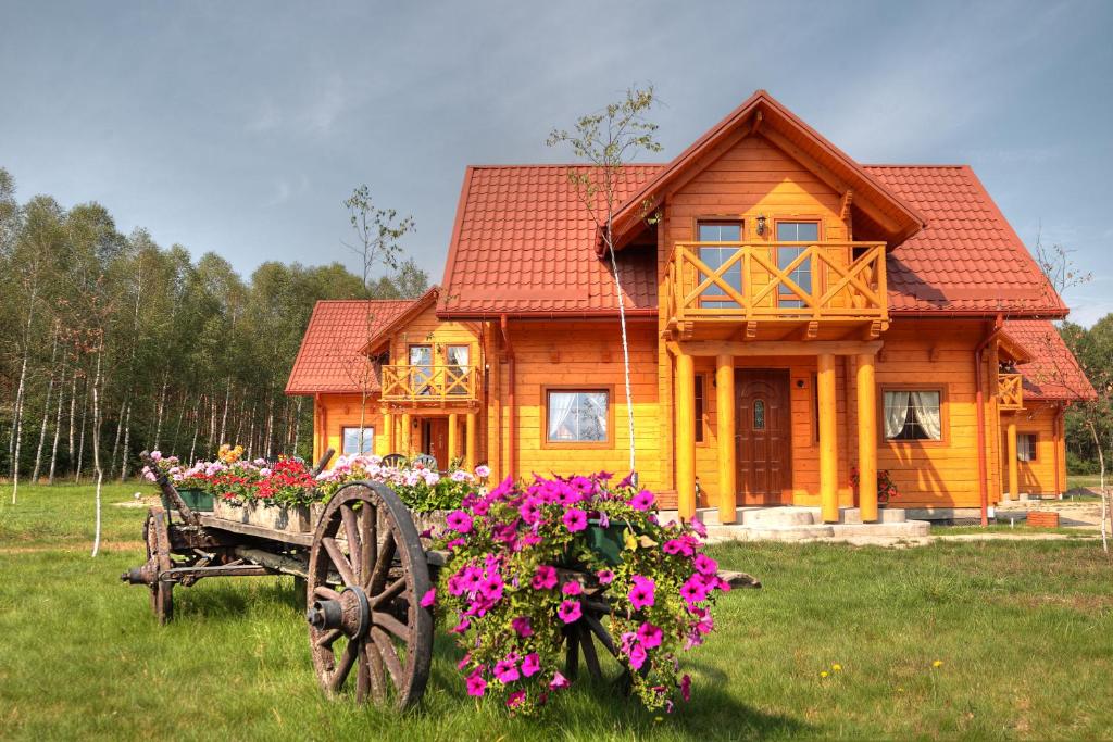 a wooden house with a cart with flowers in front of it at Ośrodek Wypoczynkowy Ranczo in Okuninka