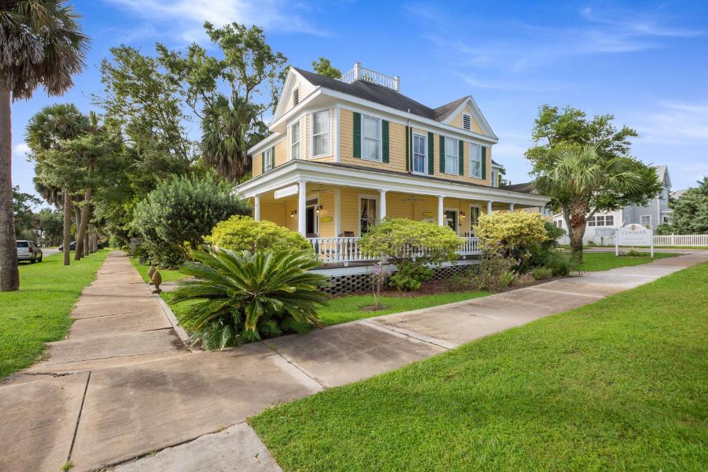 a yellow house with a porch and a sidewalk at Coombs Inn & Suites in Apalachicola