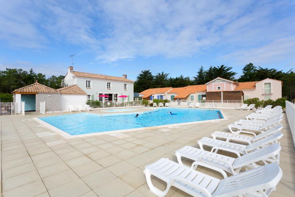 a group of white lounge chairs next to a swimming pool at Madame Vacances les Mas de Saint Hilaire in Saint-Hilaire-de-Riez