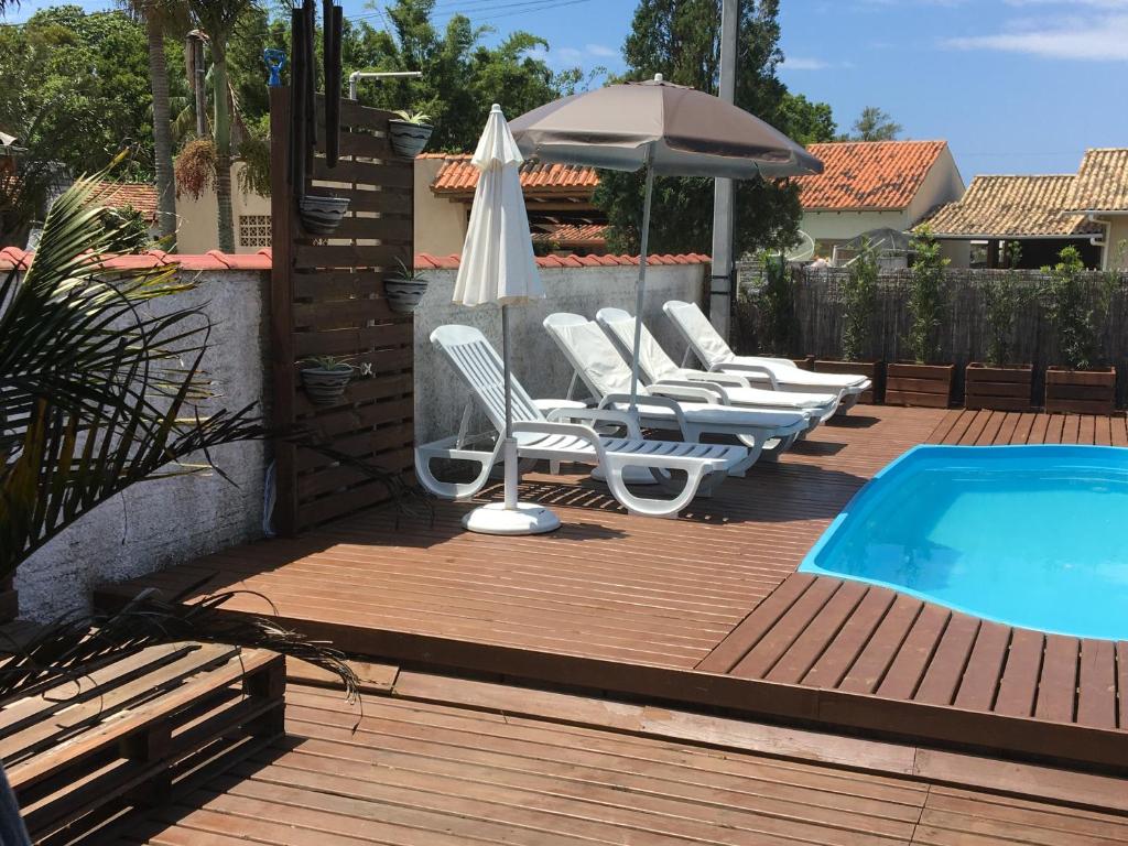 una terraza con sillas y una sombrilla junto a la piscina en Casa aconchegante, en Imbituba