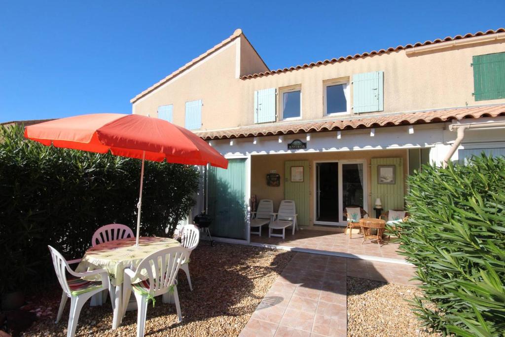 - une table et des chaises avec un parasol en face d'une maison dans l'établissement Belle villa 2 chambres, vue réserve, résidence avec piscine commune à 800m de la mer PORTIRAGNES plage LRCS114, à Portiragnes