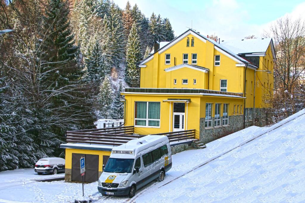 une camionnette garée devant une maison jaune dans la neige dans l'établissement Hotel Astoria with private skibus, à Janské Lázně