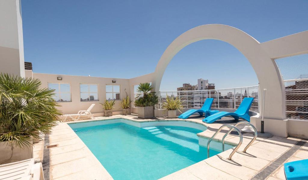 uma piscina no telhado de um edifício com cadeiras azuis em Urquiza Apart Hotel & Suites em Rosário