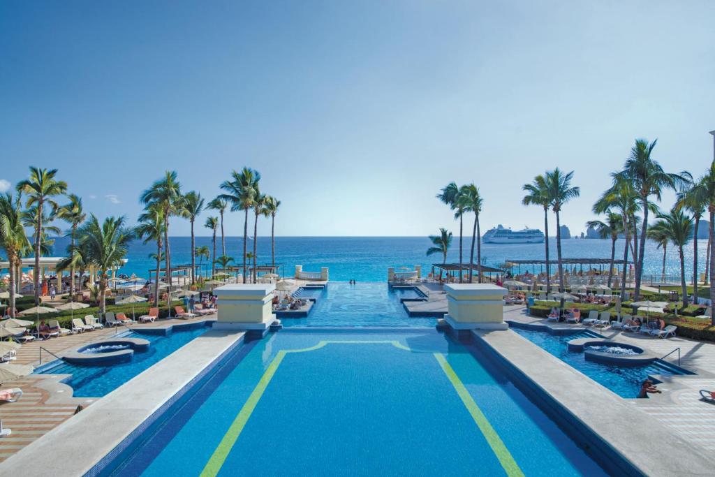 uma piscina num resort com palmeiras e o oceano em Riu Palace Cabo San Lucas - All Inclusive em Cabo San Lucas